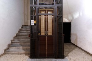 A metal gate with a sign indicating a lift area, a staircase, and a wall with a textured surface. - Casa Linnéa Vacanze, Central apartment, WIFI, Printer & Scanner, A/C, heating (Roma)