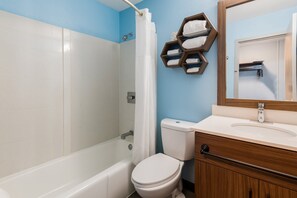 A bathroom with a shower, toilet, and vanity with a mirror. - HomeTowne Studios By Red Roof Newport News – Hampton West (Newport News)