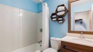 A bathroom with a shower, toilet, and vanity with a mirror. - HomeTowne Studios By Red Roof Newport News – Hampton West (Newport News)
