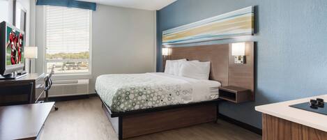 Una habitación de hotel con cama, mesita de noche, escritorio y televisión.