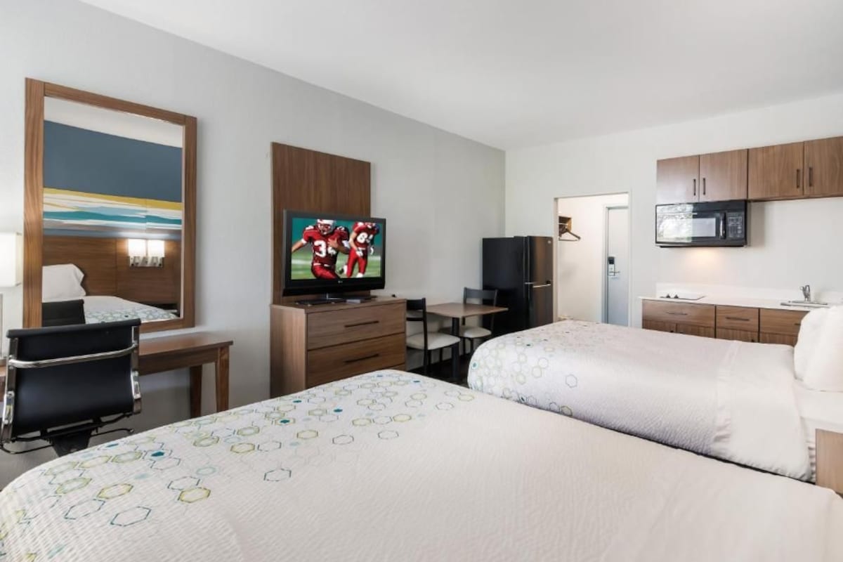 A hotel room with two beds, a desk, a television, a refrigerator, and a microwave.