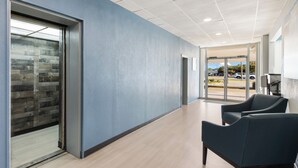 A modern hallway with a blue wall, wooden flooring, and two dark blue chairs. - HomeTowne Studios By Red Roof Newport News – Hampton West (Newport News)