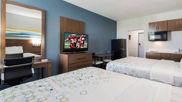 A hotel room with two beds, a TV, a desk, a chair, a microwave, and a refrigerator. - HomeTowne Studios By Red Roof Newport News – Hampton West (Newport News)