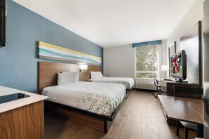 Habitación de hotel con cama, mesitas de noche, escritorio, televisor y ventana con vistas.