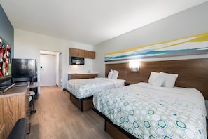 A hotel room with two beds, a desk, a TV, a microwave, and a bathroom.