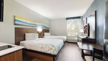 A hotel room with two beds, a desk, a chair, a TV, and a window with blinds.