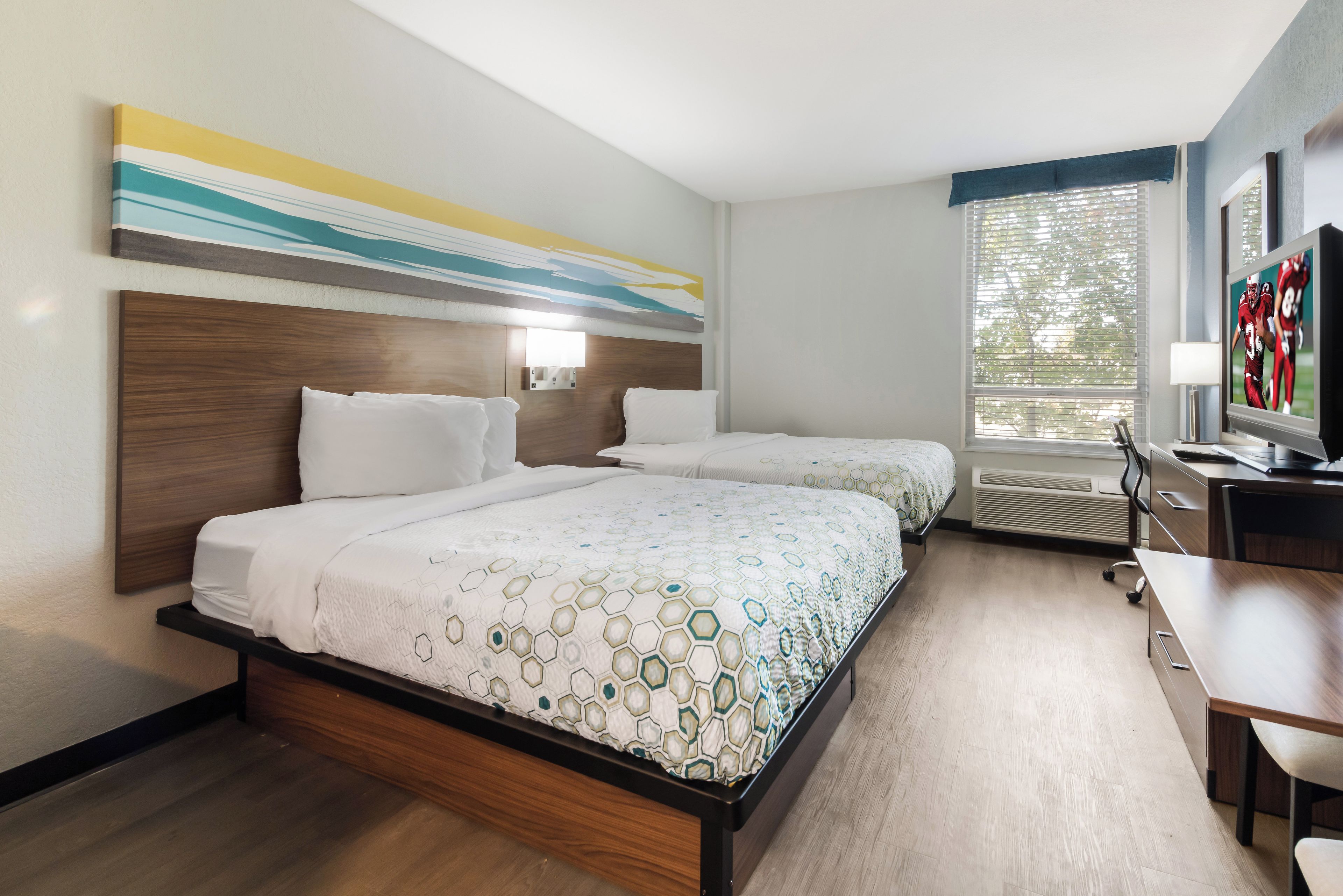 A hotel room with two beds, a desk, and a television.