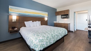 A modern hotel room with a large bed, a built-in desk, a microwave, and a sink. - HomeTowne Studios By Red Roof Newport News – Hampton West (Newport News)