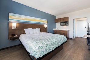 A modern hotel room with a large bed, a built-in desk, a microwave, and a sink. - HomeTowne Studios By Red Roof Newport News – Hampton West (Newport News)