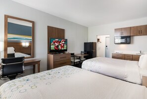A hotel room with two beds, a desk, a television, a microwave, and a small kitchenette. - HomeTowne Studios By Red Roof Newport News – Hampton West (Newport News)