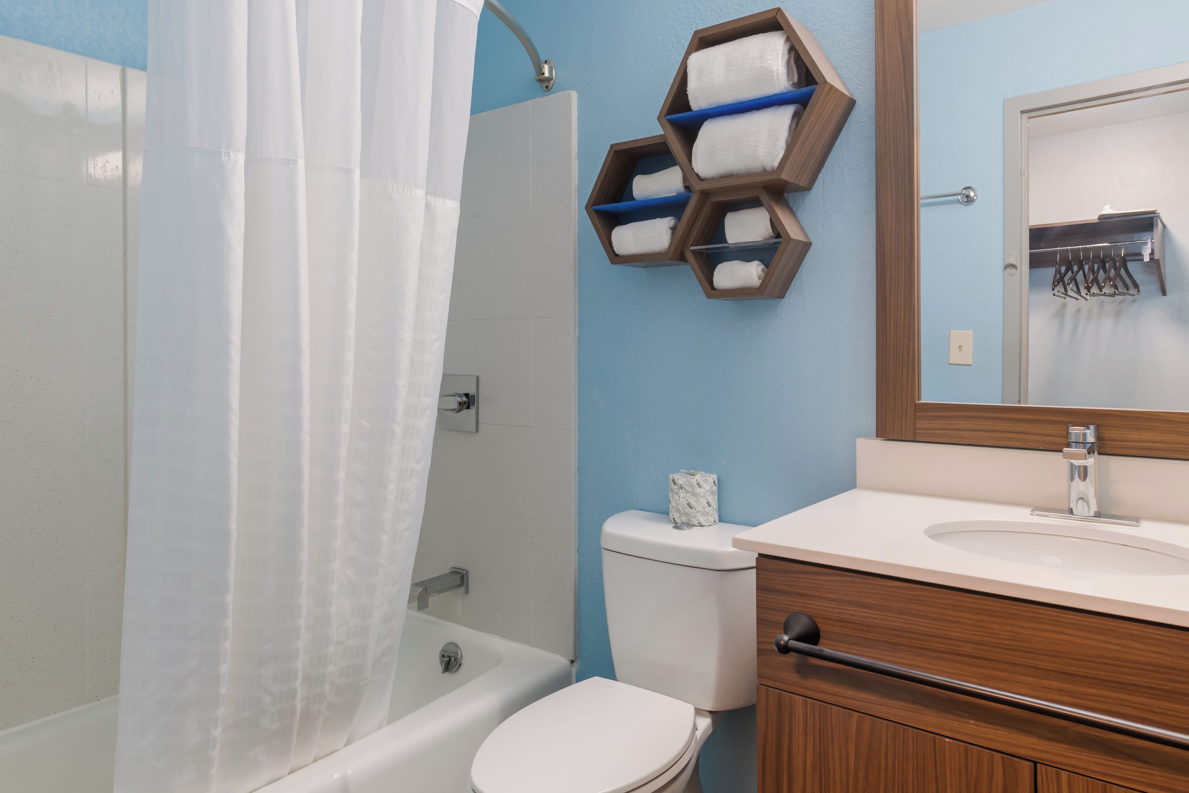 Une salle de bain équipée d’un rideau de douche, de toilettes, d’un lavabo et d’un porte-serviettes doté d’étagères hexagonales.