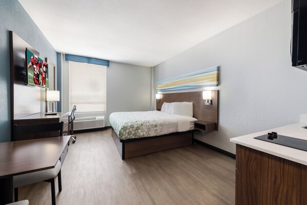 Habitación de hotel con cama, escritorio, silla, televisor y ventana con persianas.
