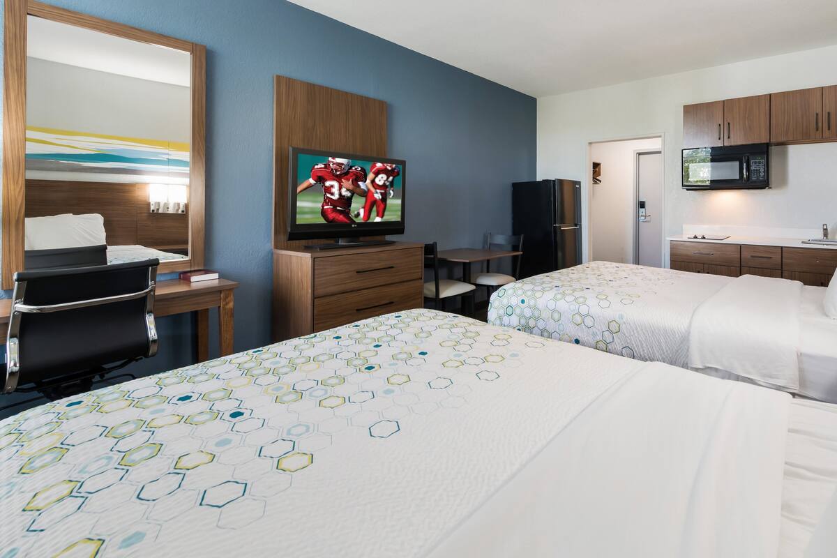A hotel room with two beds, a TV, a desk, a chair, a microwave, and a refrigerator.