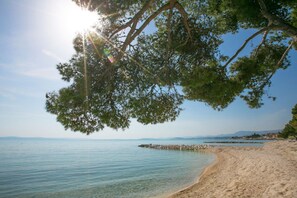 A beach with clear water, a sandy shore, and a rocky outcrop in the distance.