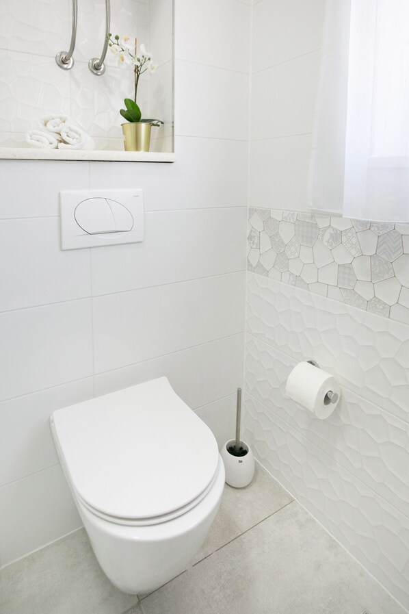 A modern bathroom with a toilet, a toilet paper holder, a hand dryer, and a small potted plant on the sink counter.