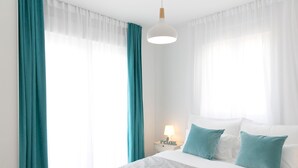 Et hotelværelse med en seng, turkise gardiner, en hvid lampe og en hvid loftslyse.
