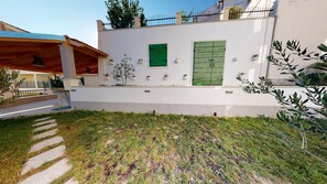 Una casa moderna con fachada blanca, contraventanas verdes y un pequeño jardín con piedras que conducen a un porche cubierto.