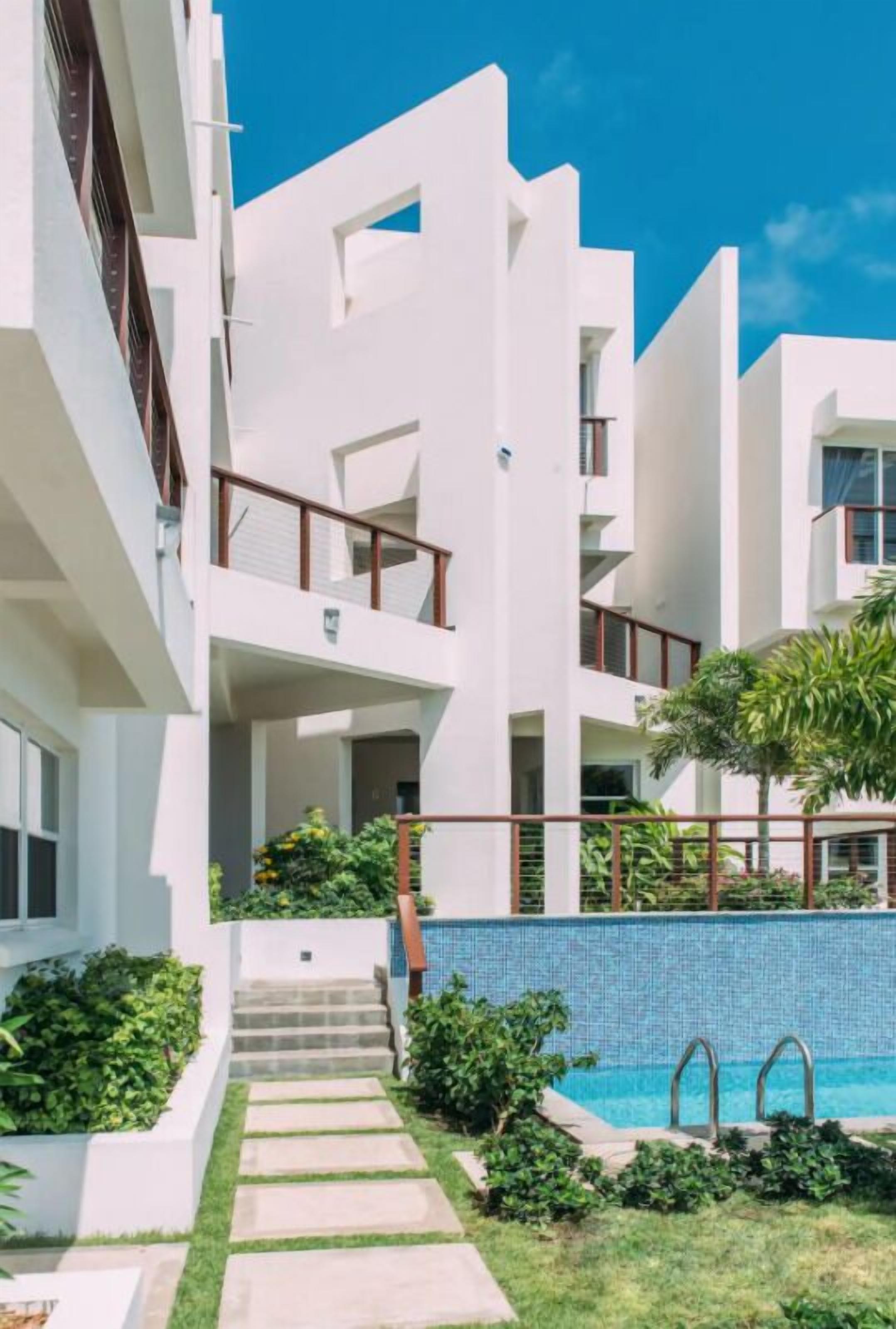 A modern multi-story building with balconies, a swimming pool, and a well-maintained garden.