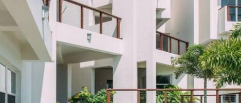 A modern multi-story building with balconies, a swimming pool, and a well-maintained garden.