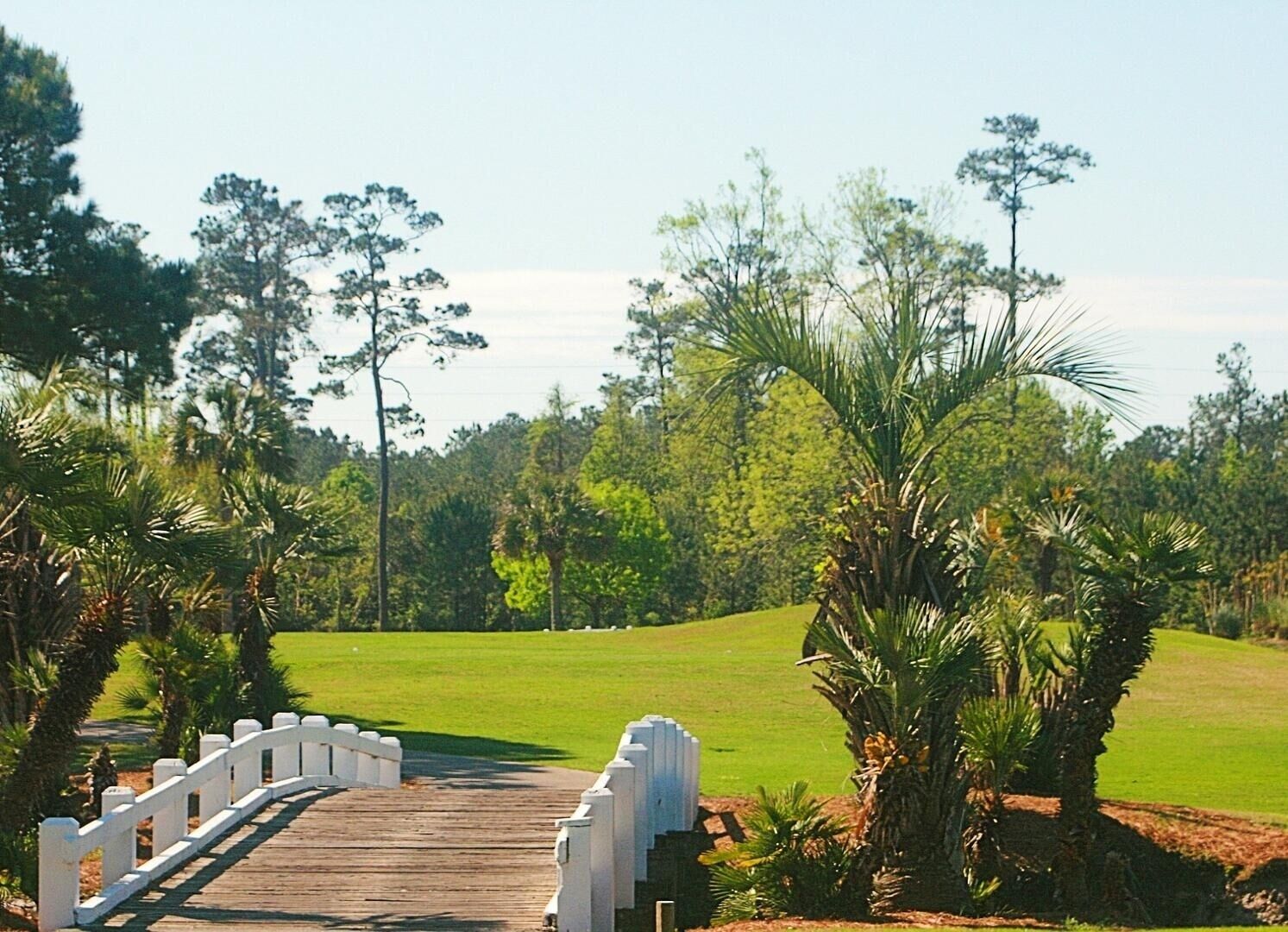 Eine Holzbrücke mit weißen Geländern, die zu einem Golfplatz führt.