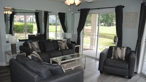A modern living room with a sectional sofa, a glass coffee table, and a view of a garden through large sliding glass doors. - 503 2 Bedroom Villa by RedAwning (Calabash)