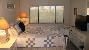 Un dormitorio con cama, mesita de noche, lámpara, televisión y ventana con vistas a zonas verdes.