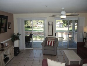 Una sala de estar con ventilador de techo, chimenea, puerta corrediza que da a un patio y vistas a una zona residencial.