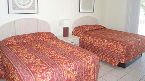 Een hotelkamer met twee bedden, een nachtkastje, een lamp en twee ingelijste kunstwerken aan de muur.