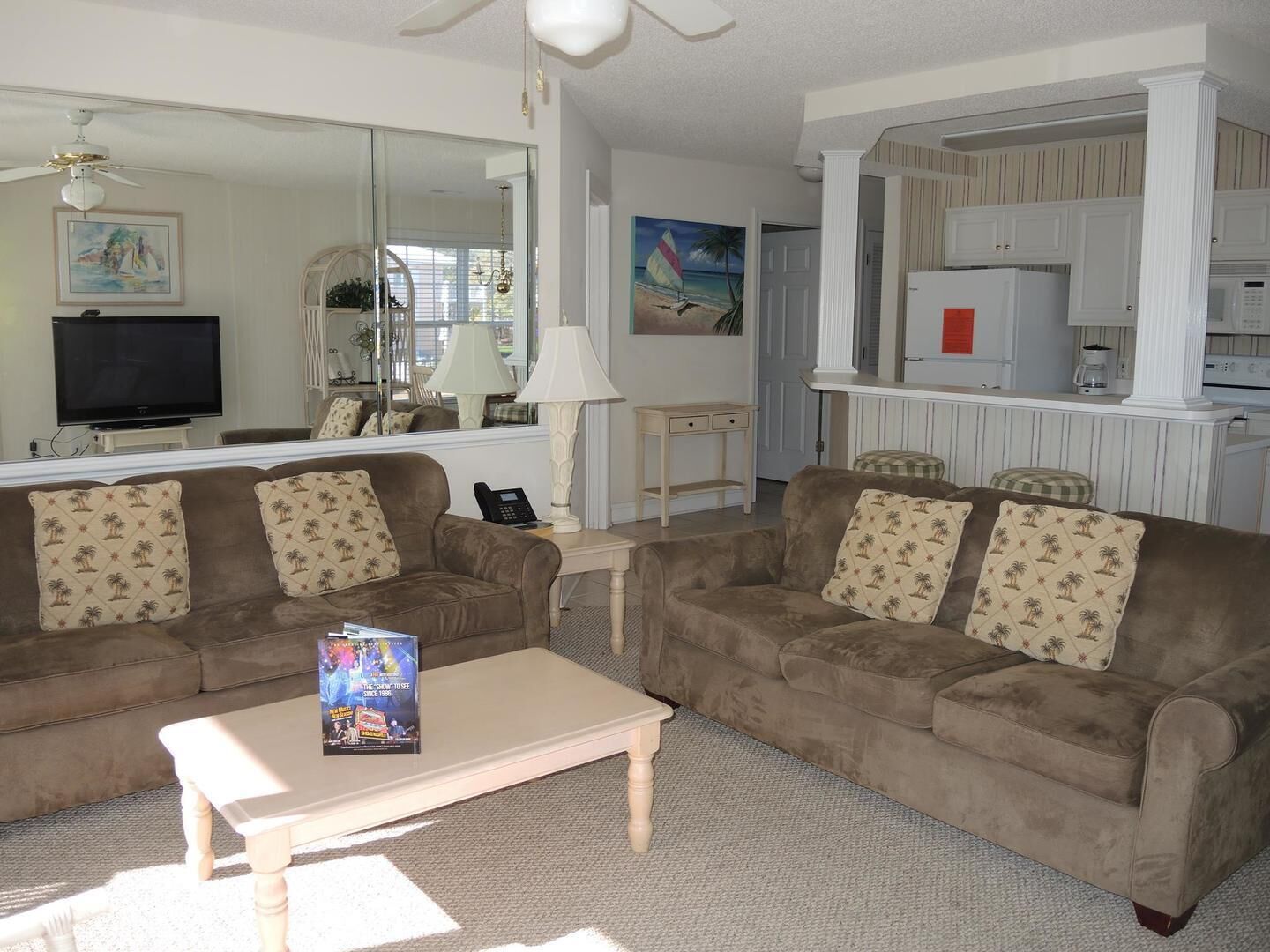 A living room with two sofas, a coffee table, a TV, a lamp, and a kitchen area with a refrigerator and microwave.
