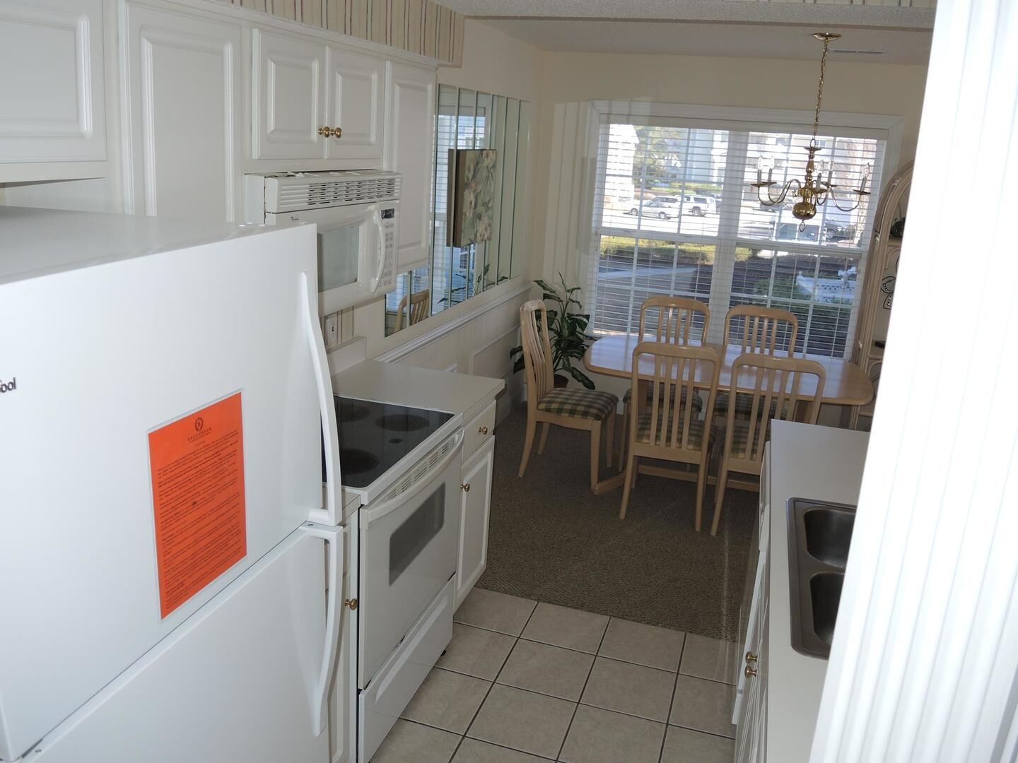 A compact kitchen with white cabinetry, a built-in oven, a microwave, and a dining area with wooden chairs and a table.