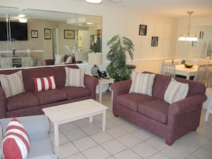 A living room with two sofas, a coffee table, and a dining area with a table and chairs. - 2705 2 Bedroom Villa by RedAwning (Calabash)