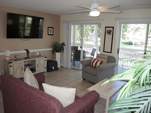 Een woonkamer met een televisie, een plafondventilator, een bank, een stoel en een tafel.