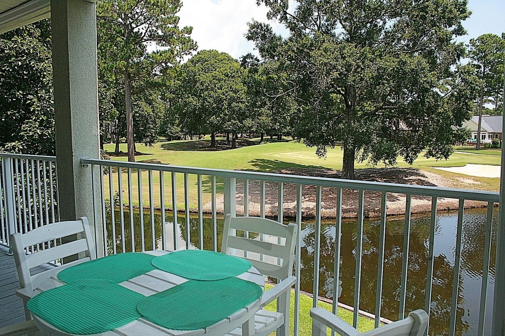 A balcony with a table and chairs, overlooking a golf course and a pond.