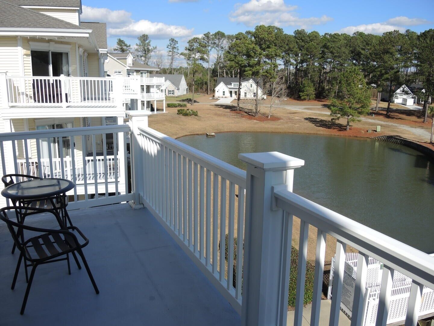 A balcony with a view of a lake, a small table, and chairs.