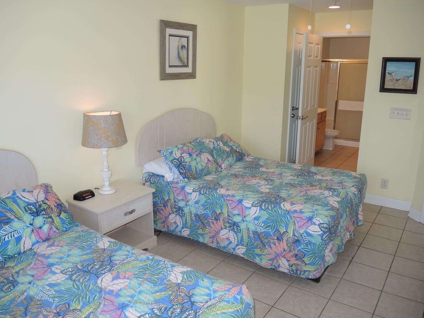 Une chambre avec deux lits, une table de chevet, une lampe et une porte donnant sur une salle de bain.