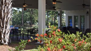 Un patio extérieur couvert, doté de plusieurs ventilateurs de plafond, de chaises en métal noir et d’une table à manger.