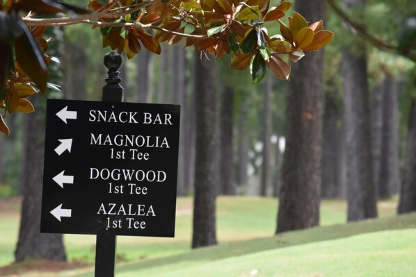 Una señal direccional con flechas que indican varios lugares, incluyendo un bar de aperitivos, Magnolia, Dogwood y Azalea.