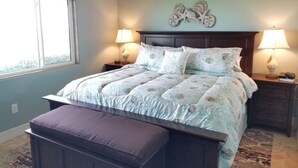 Un dormitorio con una cama grande, dos mesitas de noche con lámparas, una ventana y un elemento decorativo en la pared.