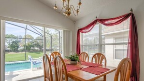 A dining area with a table and chairs, a chandelier, and a view of a swimming pool and greenery outside. - Gated Community Private Pool 3 Bedroom Home by Redawning (Haines City)