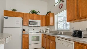 A modern kitchen with wooden cabinets, a refrigerator, microwave, stove, dishwasher, and a toaster. - Gated Community Private Pool 3 Bedroom Home by Redawning (Haines City)