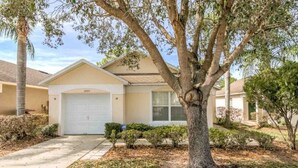 A single-story house with a garage, a tree in front, and a well-maintained lawn. - Gated Community Private Pool 3 Bedroom Home by Redawning (Haines City)