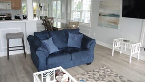 A modern living room with a dark blue sofa, a glass coffee table, and a geometric patterned rug. - Family Friendly Golf Course View Condo 101M with Great Brunswick Plantation Resort Amenities by RedAwning (Calabash)