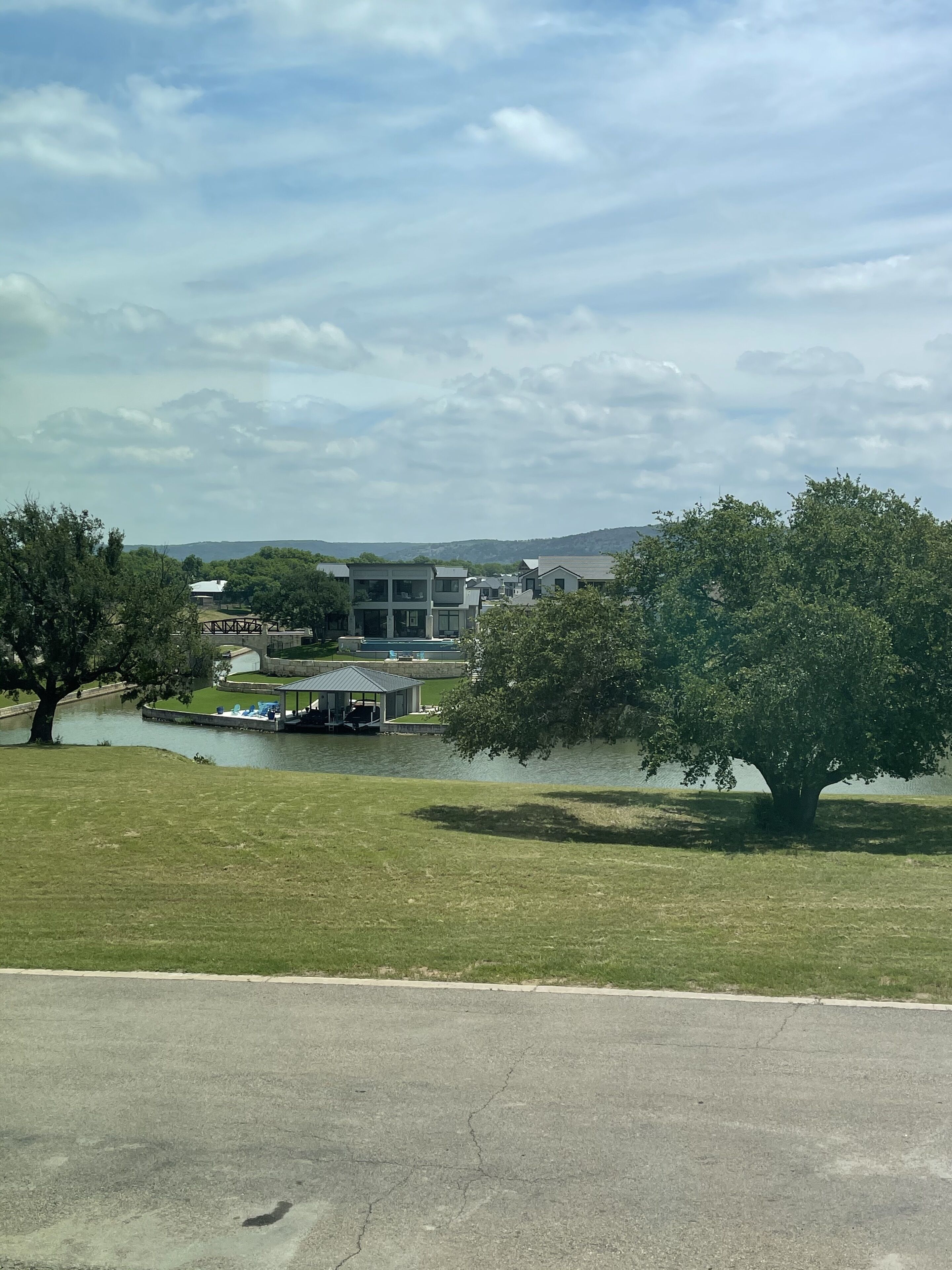 A park with a lake, trees, and a building with a gazebo and lounge chairs.