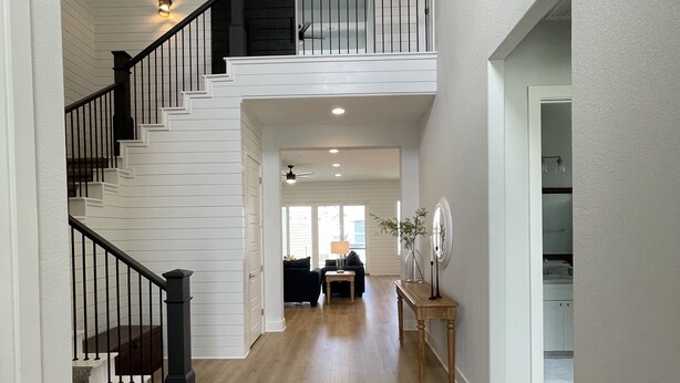 Un intérieur spacieux avec un escalier menant à un deuxième étage, un coin salon avec une table basse et une vue sur l’extérieur.