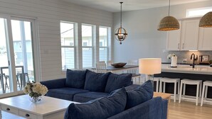 Un salon moderne avec un canapé d’angle bleu, une table basse blanche et un coin repas comprenant une table et des chaises blanches.