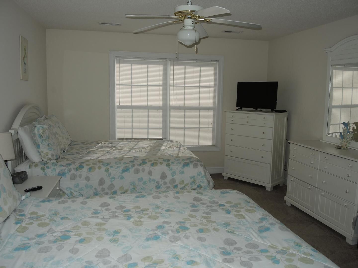 A bedroom with two beds, a ceiling fan, a dresser, and a television.