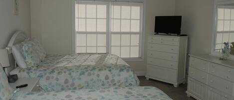 A bedroom with two beds, a ceiling fan, a dresser, and a television.