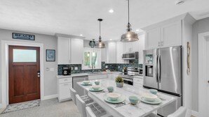 A modern kitchen with white cabinets, stainless steel appliances, and a central island with seating. - Bayside Bliss 3 Bedroom Home by RedAwning (Anna Maria)