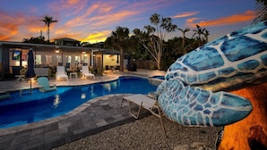 A swimming pool with lounge chairs and a modern house in the background. - Bayside Bliss 3 Bedroom Home by RedAwning (Anna Maria)