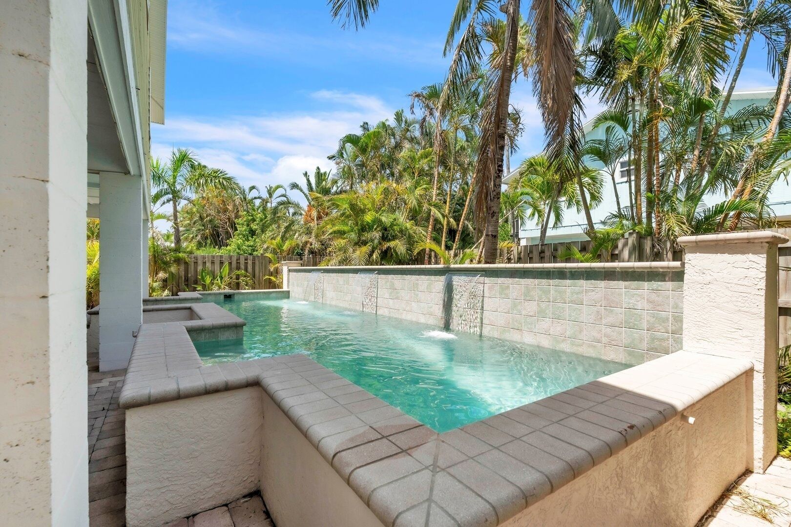 Une piscine agrémentée d’une cascade, entourée de palmiers et d’un mur de pierre.